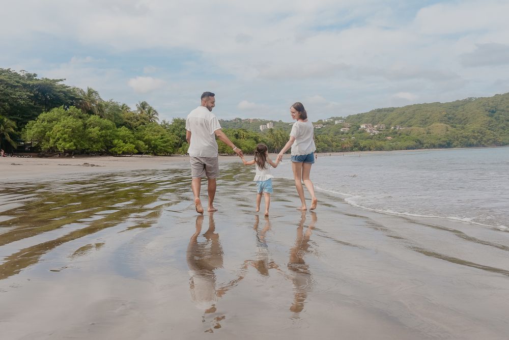 Two people walk together in shallow water along a scenic beach with mountains in the background.