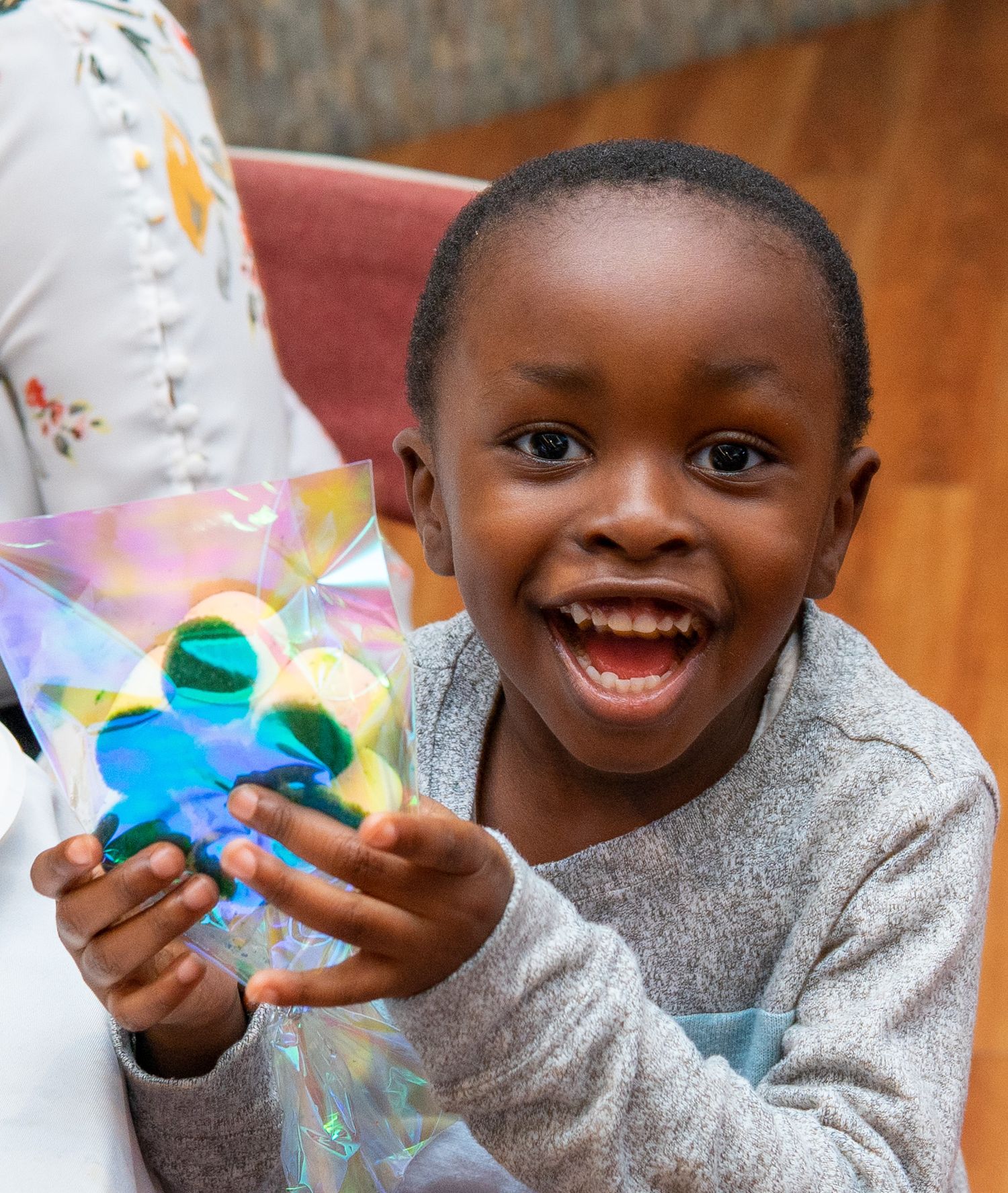 A joyful child in a grey sweater holds a colorful toy while playing.