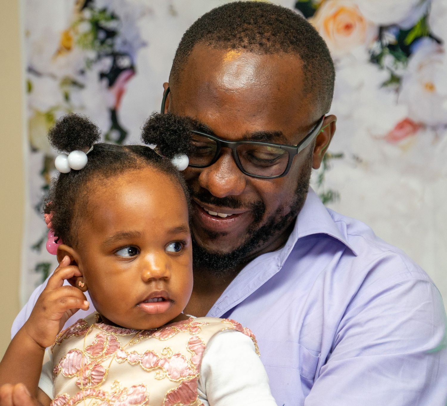 A tender moment between an adult in glasses and a small child in formal wear.