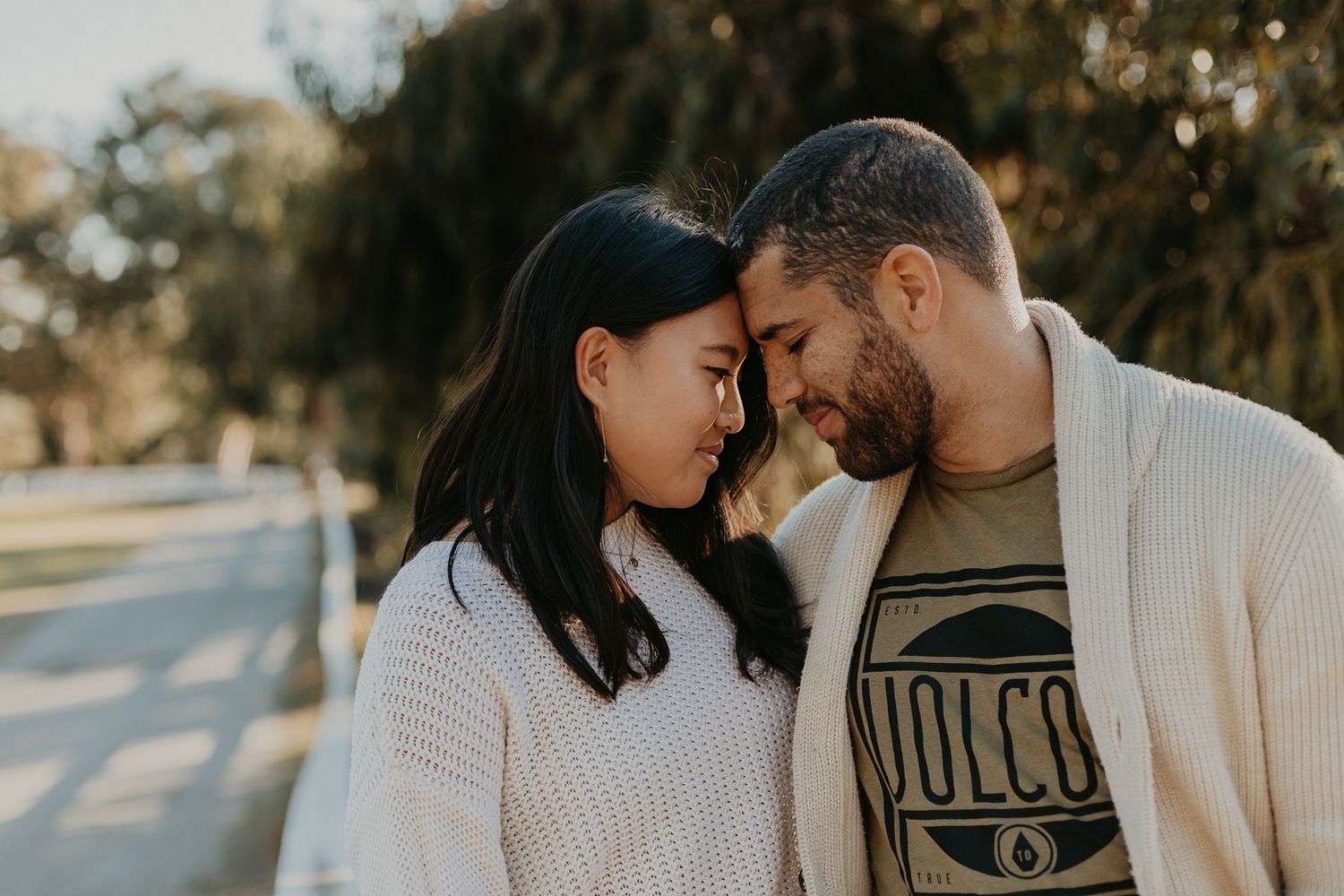 A couple in cozy white sweaters share intimate moments during a romantic outdoor photo session at sunset at Will Rogers State Park.