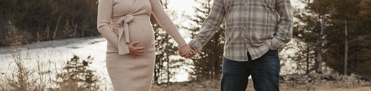 pregnant mother holds baby bump while holding husbands hand in front of a lake during photo session as date night ideas in kansas city