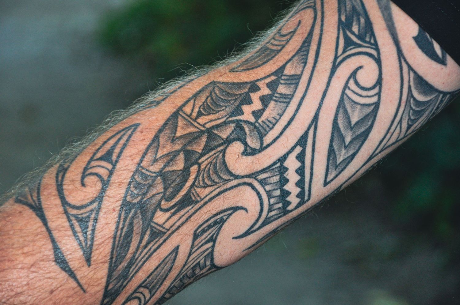Close-up of detailed black Maori tribal tattoo sleeve on forearm with geometric patterns and designs.
