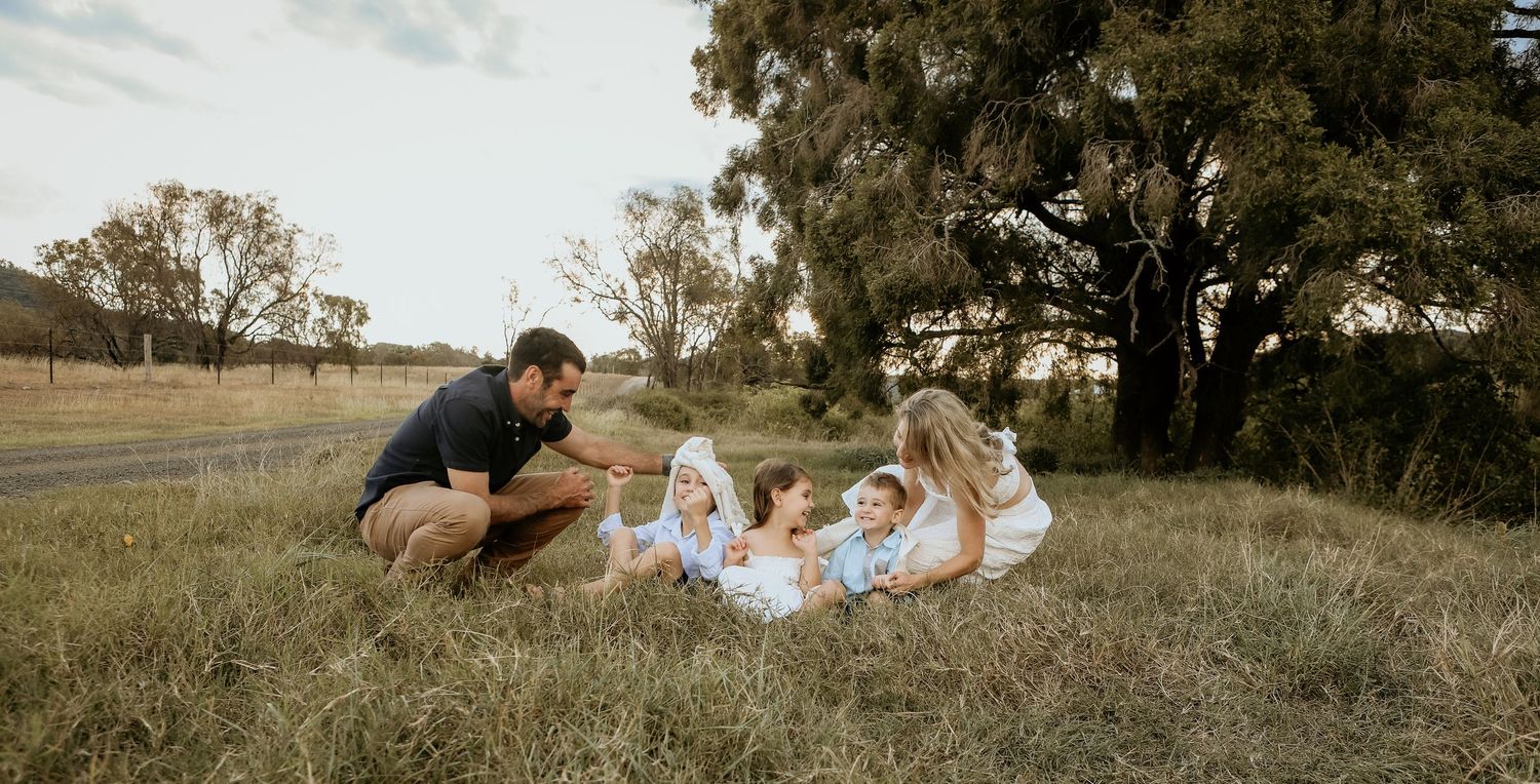 A family enjoys a candid outdoor photo session in a golden field at sunset.