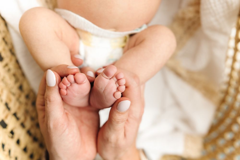 Adult hands gently hold tiny baby feet against a soft white fabric background.