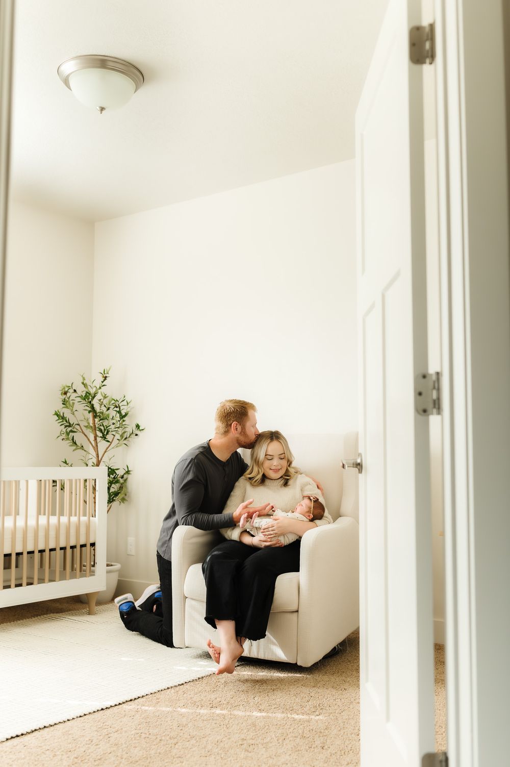 Minimalist white nursery room with mirrored panels showing a tender family moment on a white sofa.