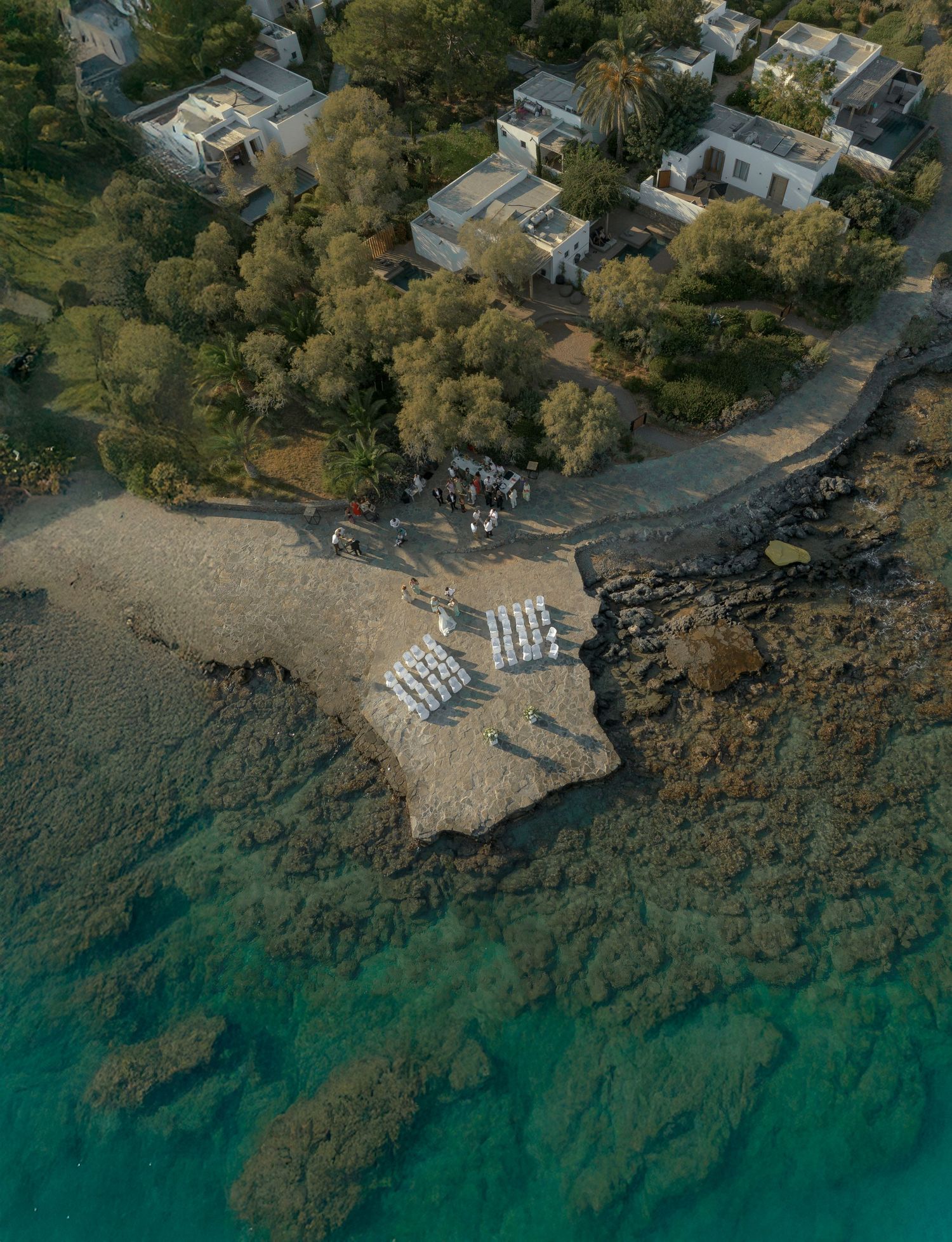 Aerial view of a small beach cove with turquoise waters and beachfront homes nestled among trees along the coastline.