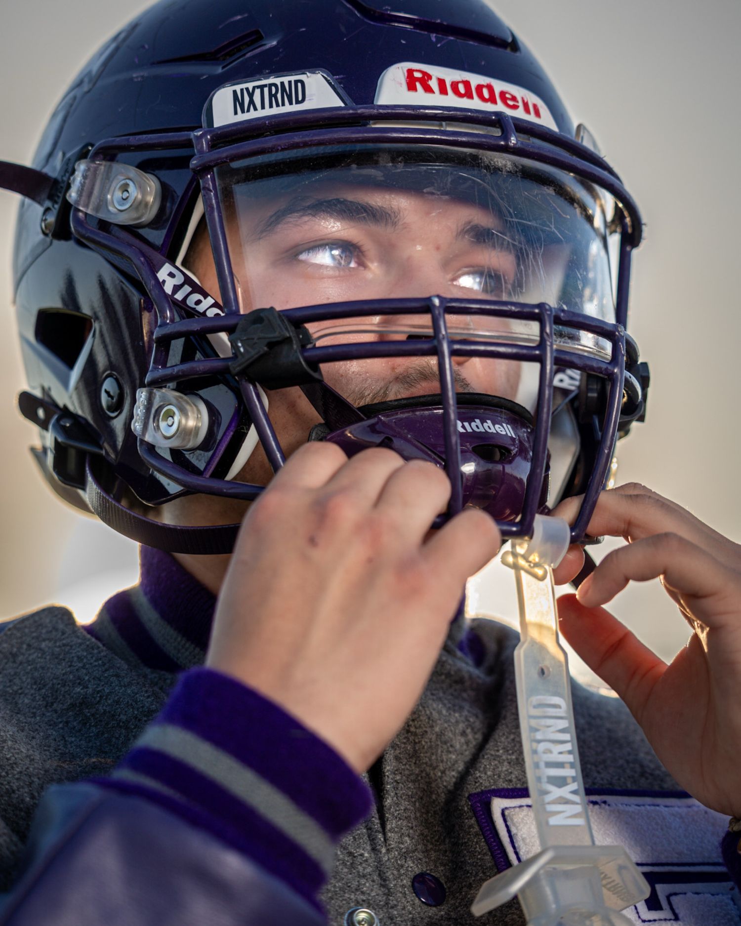 Football player adjusts protective face mask and helmet while preparing for game.