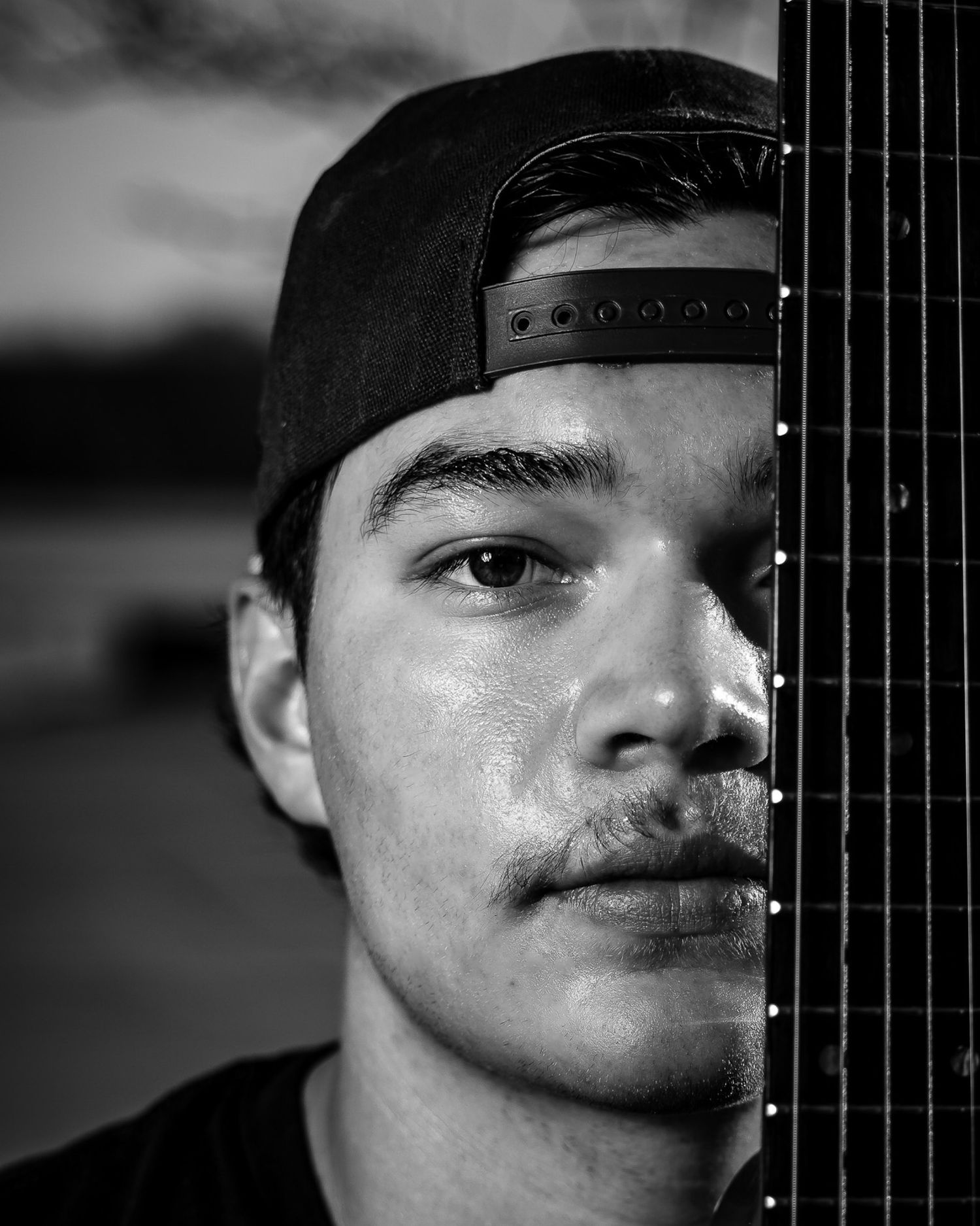 Black and white artistic portrait showing half of a face next to a musical instrument neck in shadow.