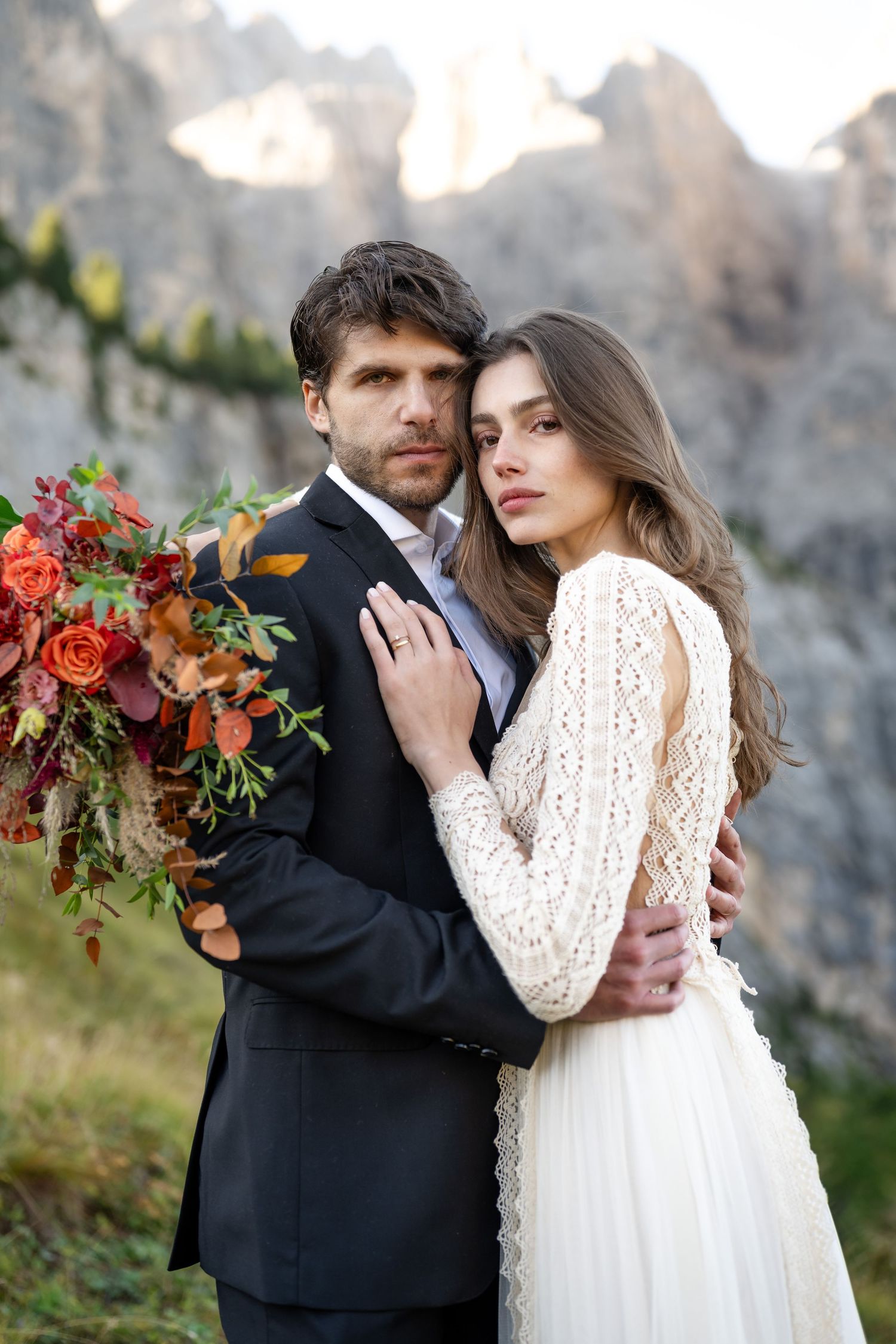 A romantic wedding couple embraces outdoors against a rocky mountain backdrop with autumn florals and elegant attire.