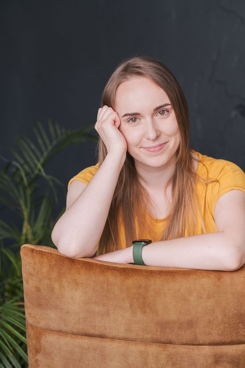 Portrait of person leaning on brown chair with plant in background.