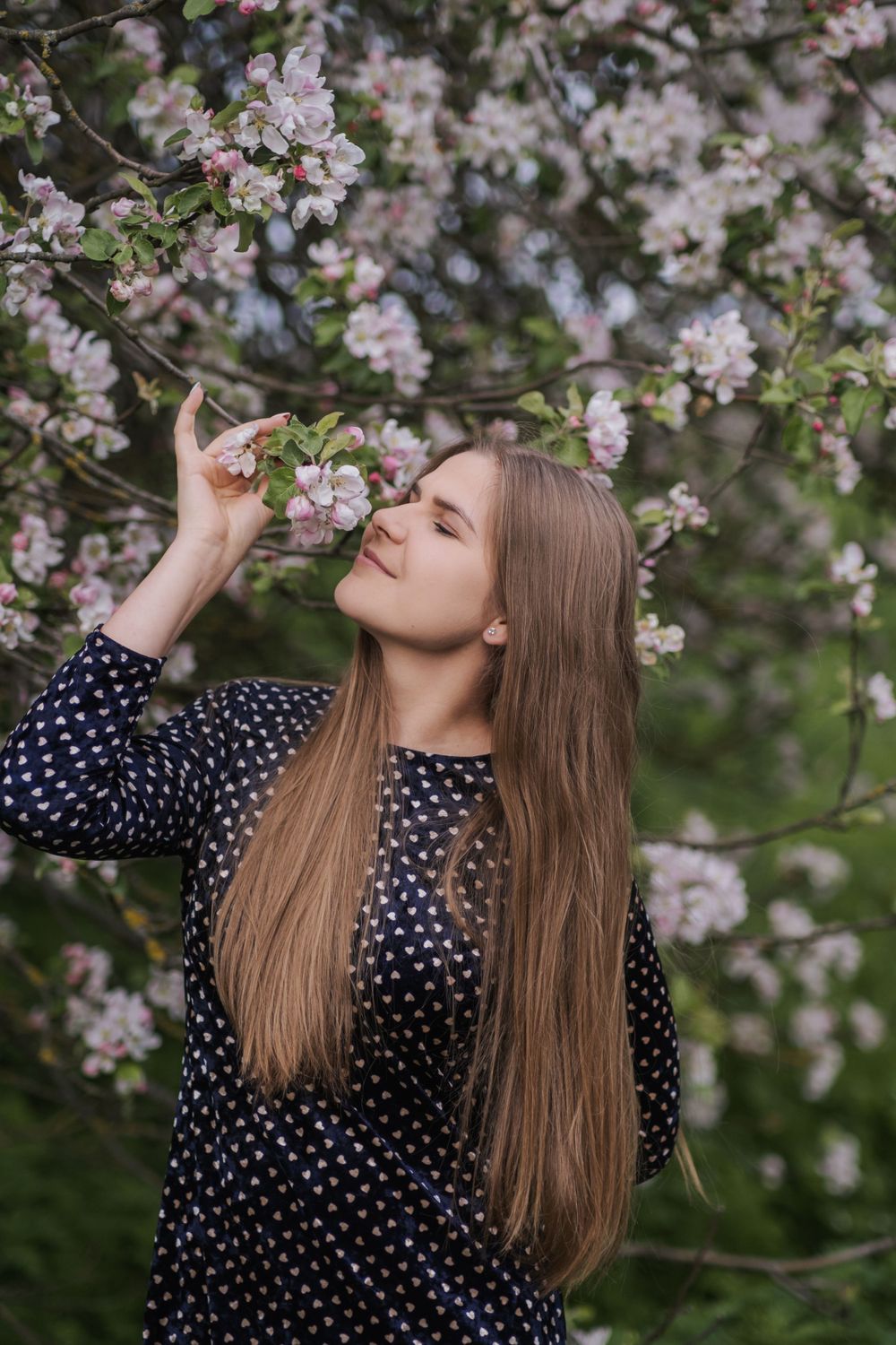 Person in polka dot dress enjoying spring cherry blossoms in garden.