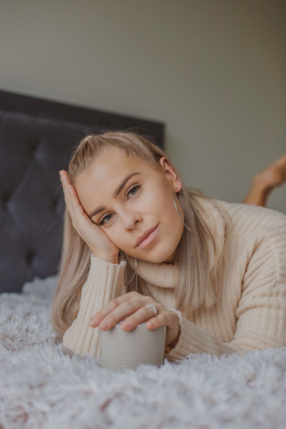 Cozy winter portrait of someone relaxing on fluffy bedding in a cream knit sweater.