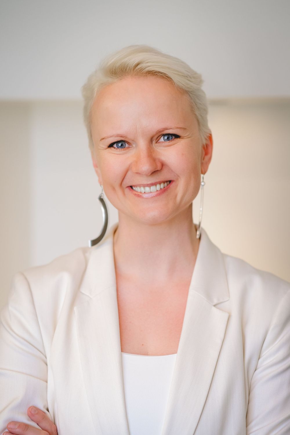 Professional portrait with crisp white blazer and short blonde hair against neutral background.