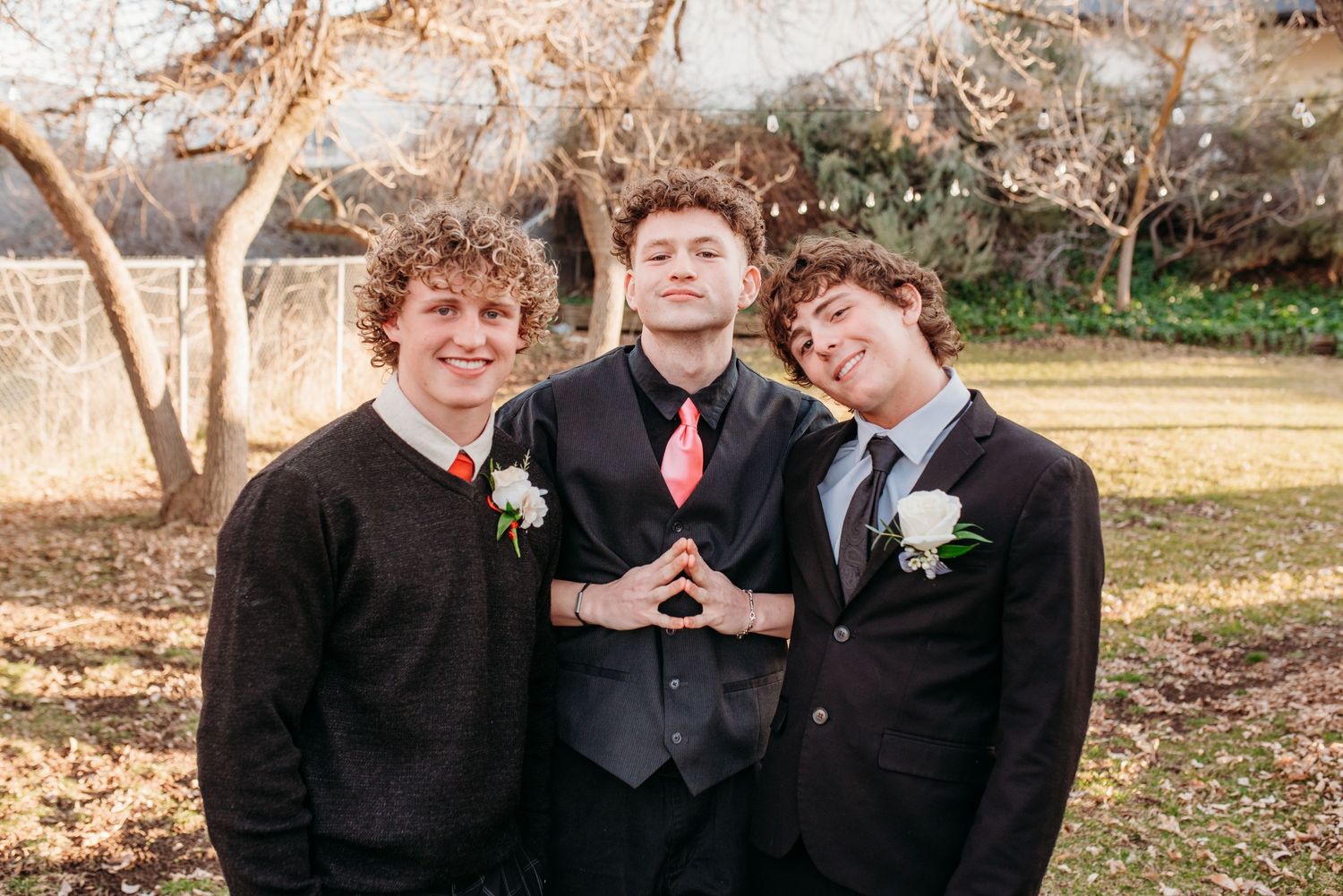 Three friends in formal wear with boutonnieres pose together outdoors in winter.