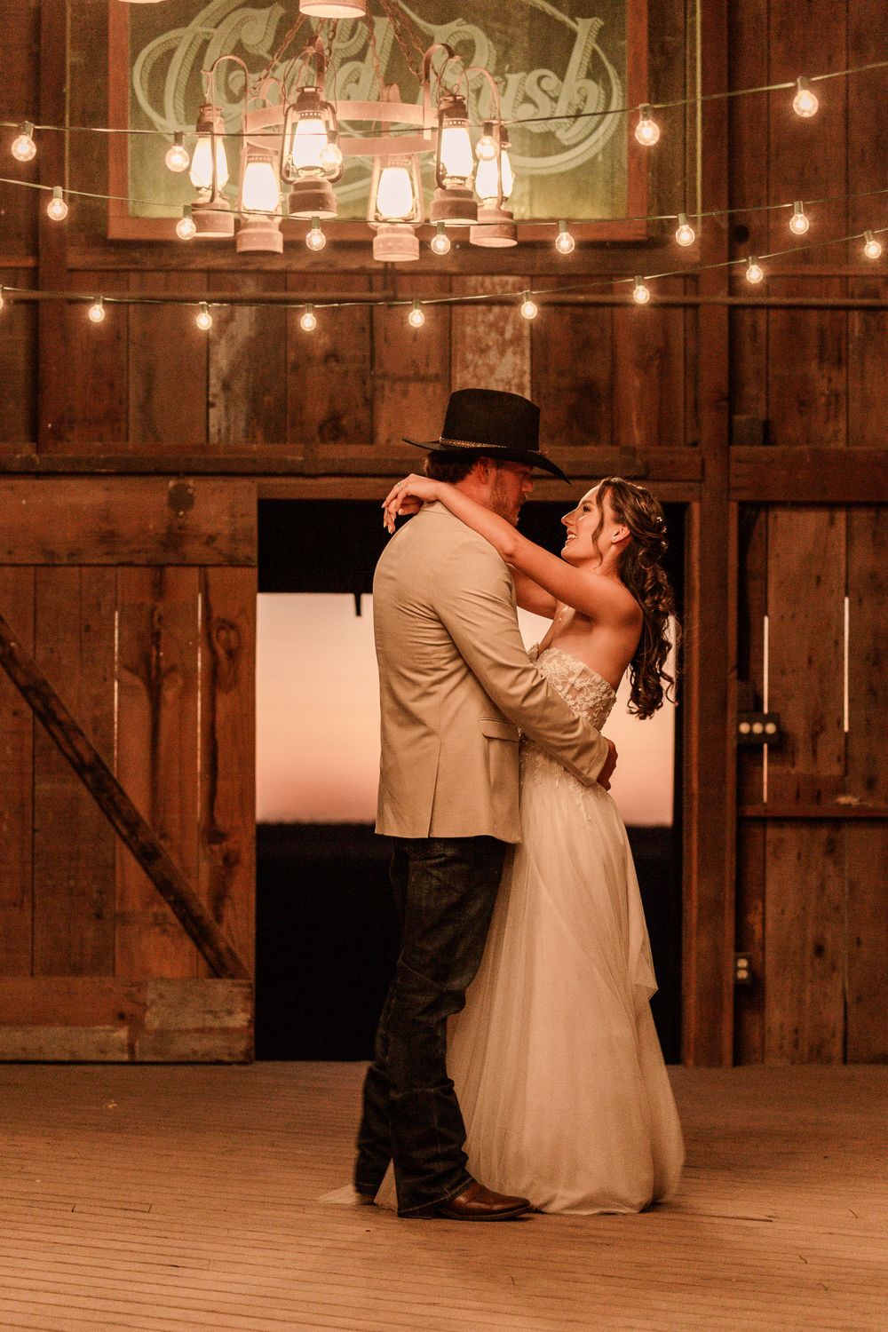 Couples slow dancing in a rustic barn venue illuminated by romantic string lights.