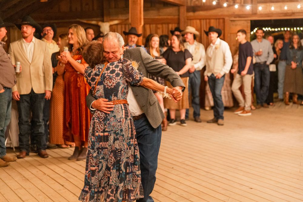 Wedding guests dancing together on a wooden dance floor in a rustic barn setting.
