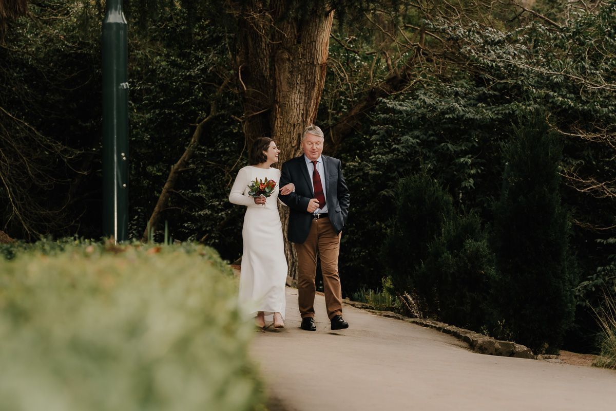 A couple walks together on a garden path surrounded by lush greenery.