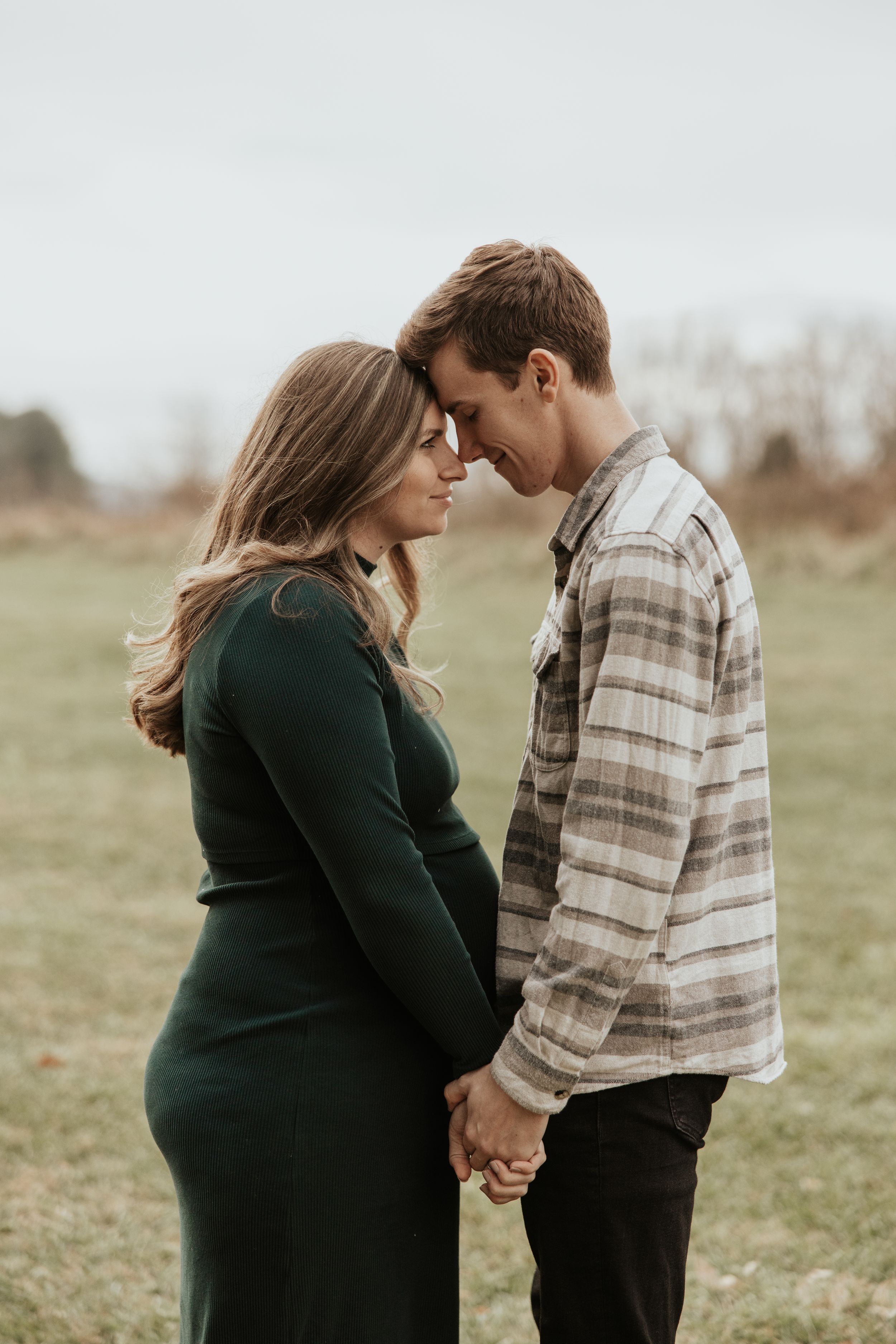 An intimate moment between a couple in a field, sharing a close embrace in muted autumn tones.