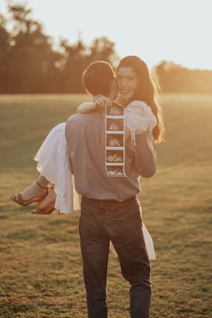 A romantic sunset moment captured as a couple embraces on a grassy hillside with warm backlighting.