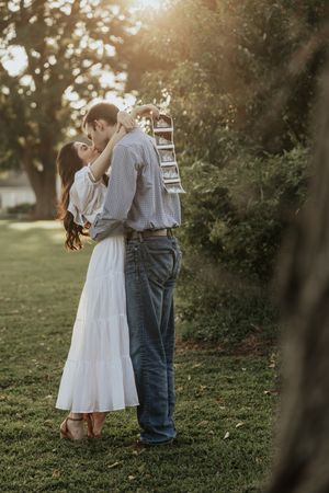 A couple dances together in a sunlit garden setting during golden hour, creating a romantic silhouette against the trees.