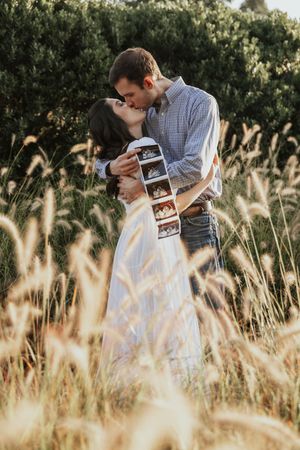Couple sitting in tall golden grass looking at ultrasound photos together during sunset.