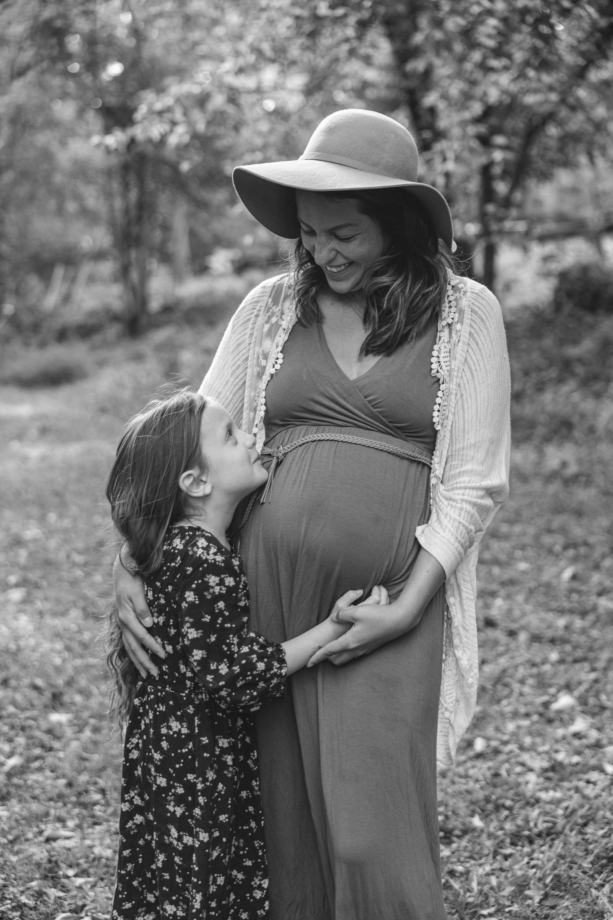 Black and white outdoor maternity photos show tender moments between mother and child in a natural setting.