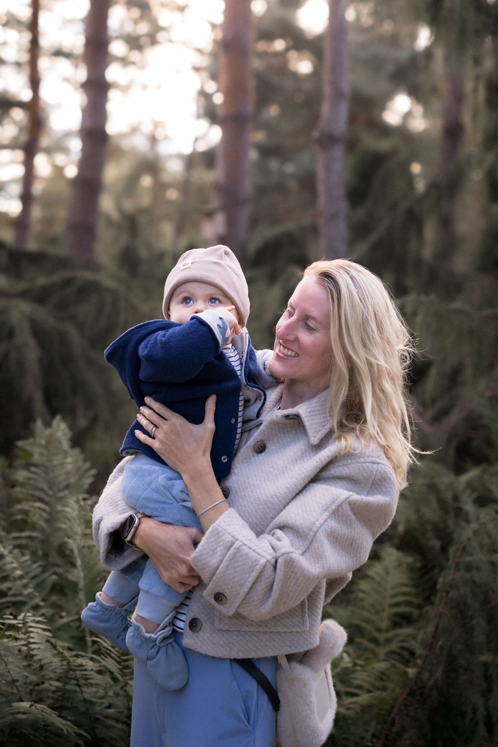 Fröhliche Fotosession im Freien, die liebevolle Eltern-Kind-Interaktionen zwischen Kiefern zeigt.