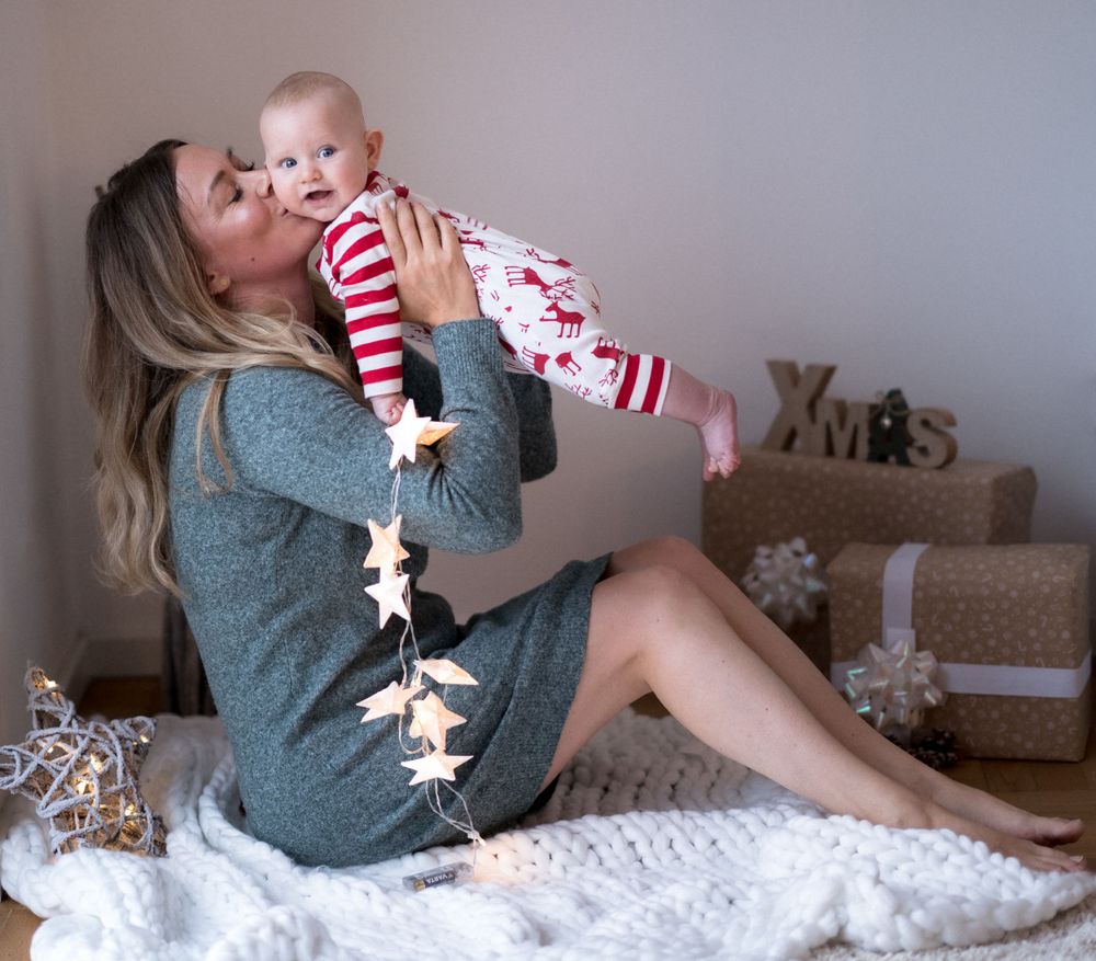 Gemütliche Lifestyle-Fotos von drinnen, die jemanden zeigen, der auf weißer Bettwäsche mit Weihnachtsdekoration entspannt.