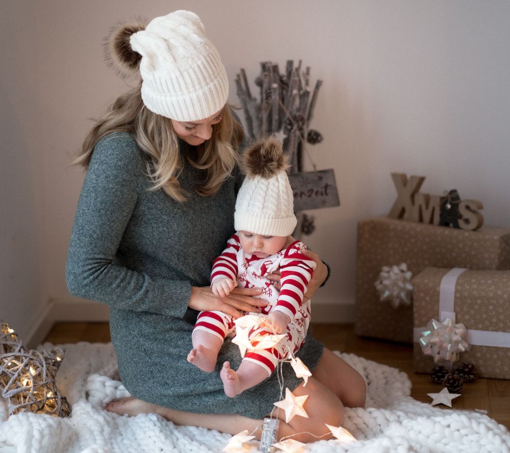 Eine festliche Feiertagsszene zeigt passende weiße Strickmützen und gemütliche Momente mit einem Baby im gestreiften Pyjama auf weißen Decke
