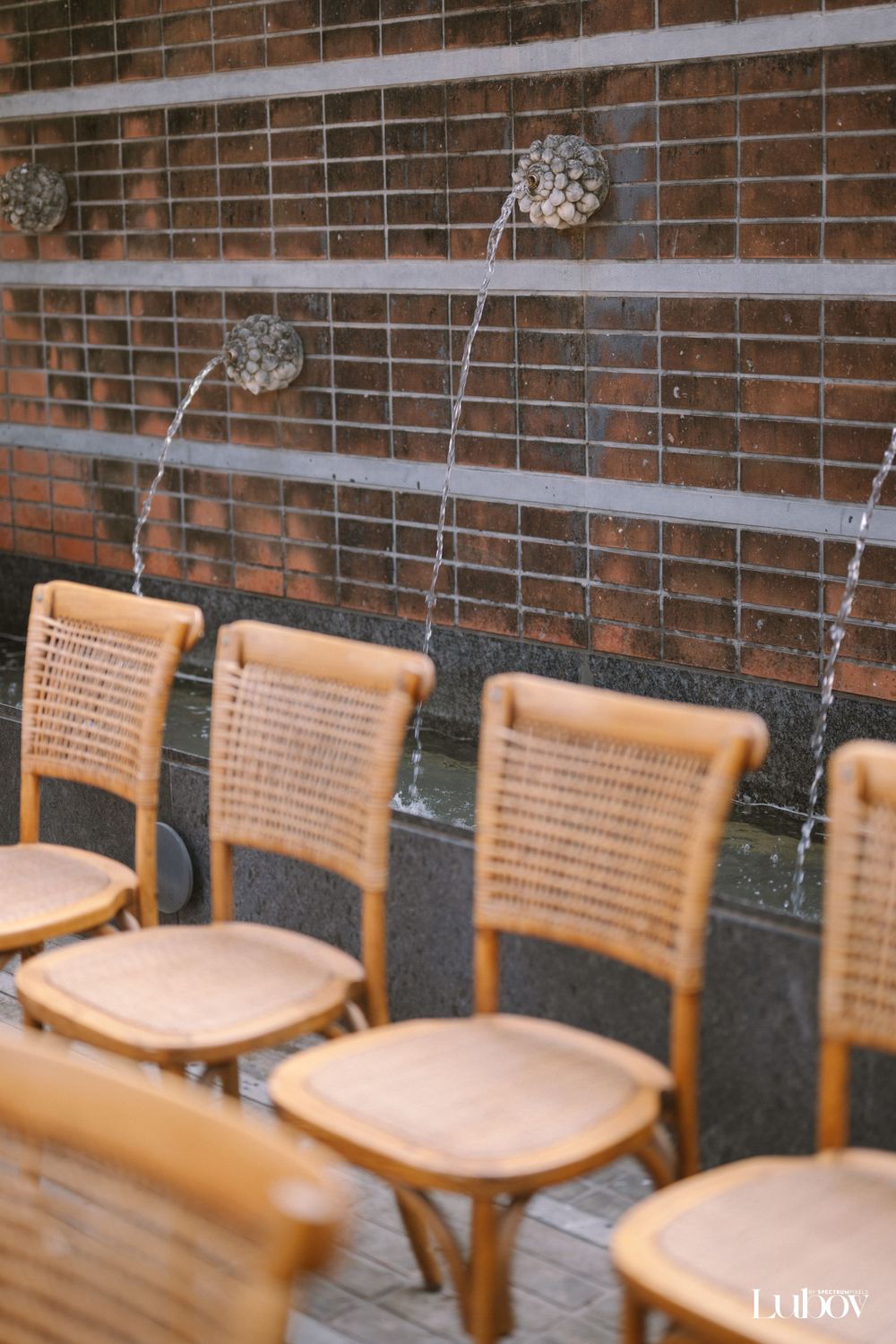 Row of vintage wooden chairs against a brick wall with hanging decorative elements.