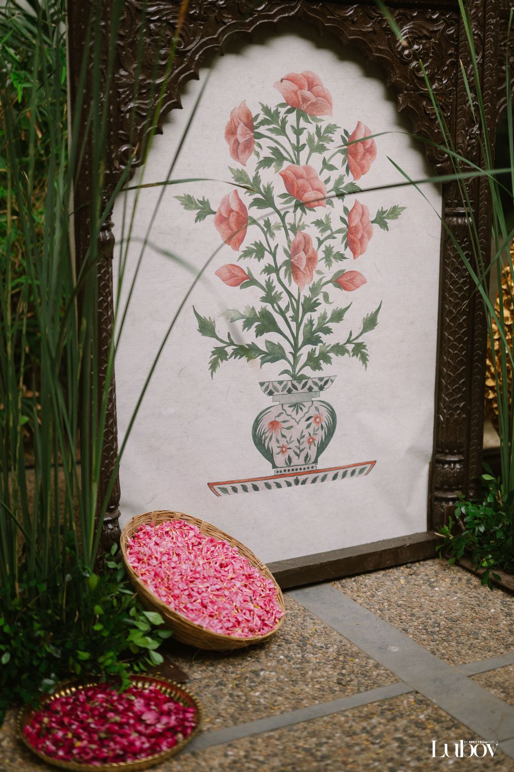 Pink floral artwork display with rose petals in copper bowls against a garden backdrop.