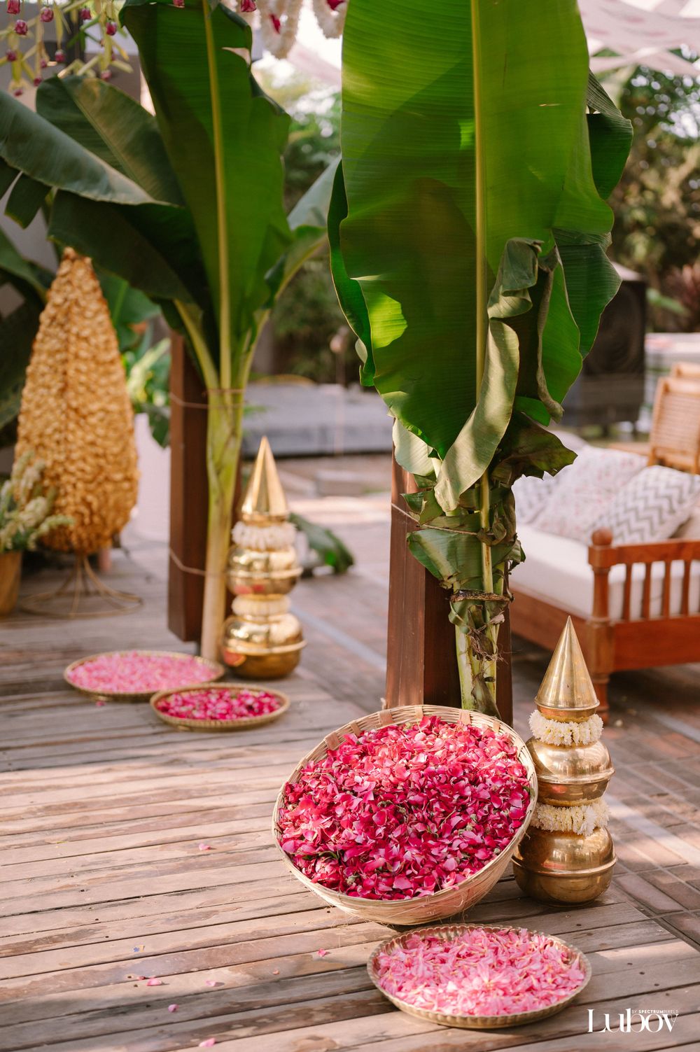 Decorative pink petals in brass bowls surrounded by tropical banana plants and gold accents.