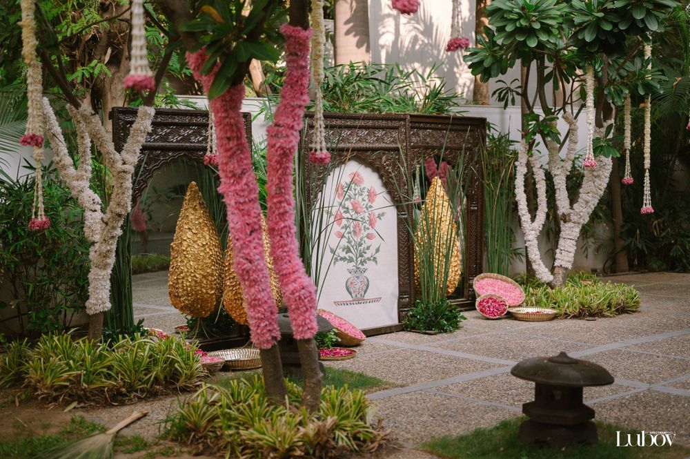 Tropical garden setting with decorative panels, gold accents, and pink-wrapped tree trunks.