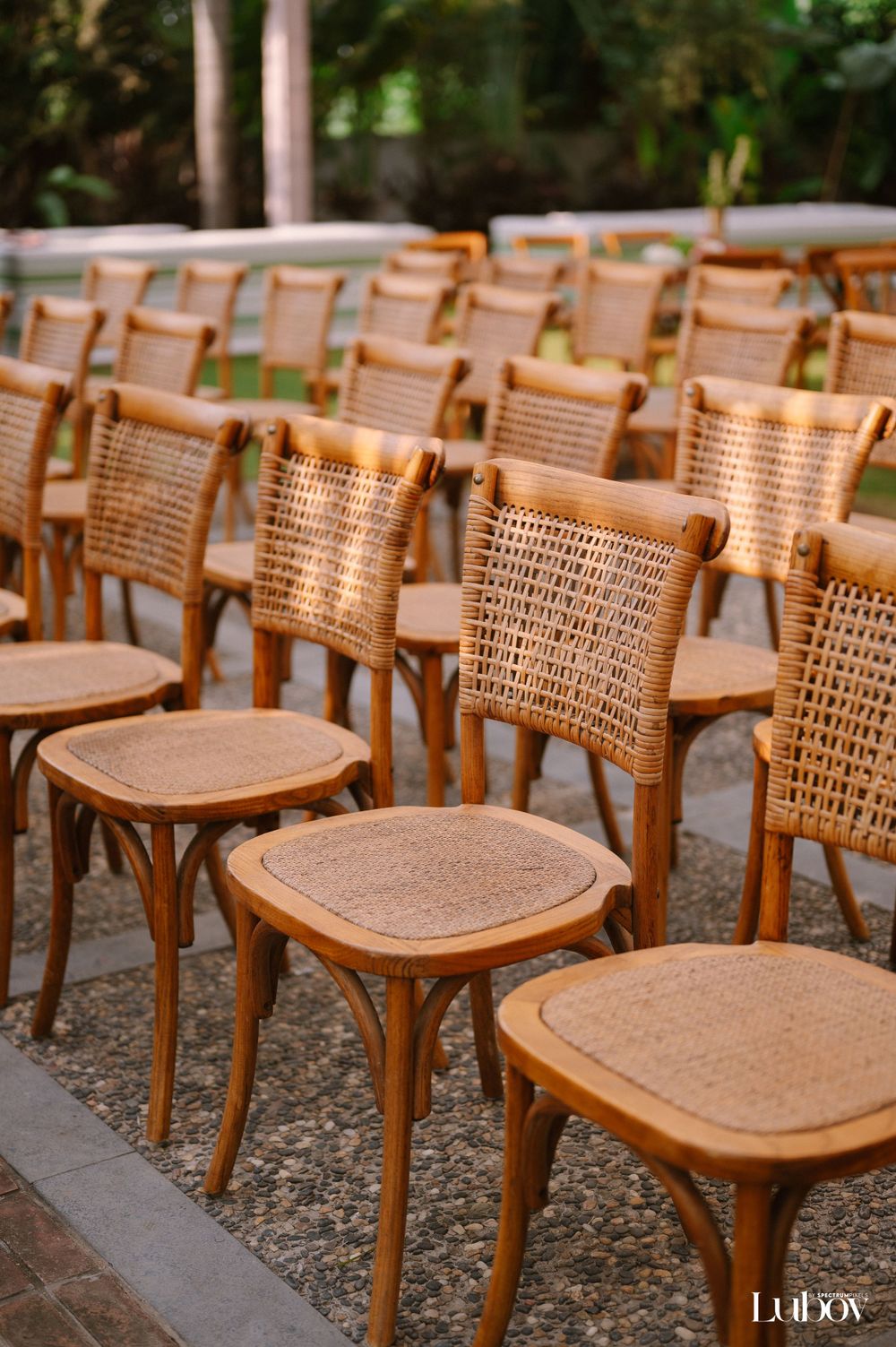Elegant arrangement of woven cane chairs set up for an outdoor wedding ceremony.