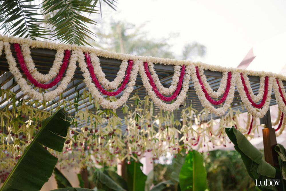 Traditional floral garland decorations hanging between palm fronds at an outdoor celebration.