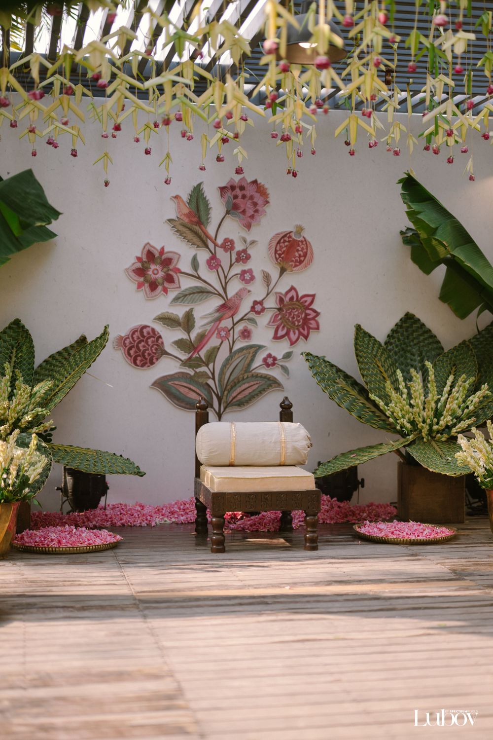 Wedding stage decor featuring floral wall art, hanging installations, and a white cushioned chair.