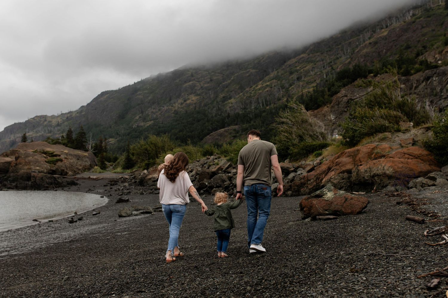 Family walking together on rocky beach with misty mountains in background.