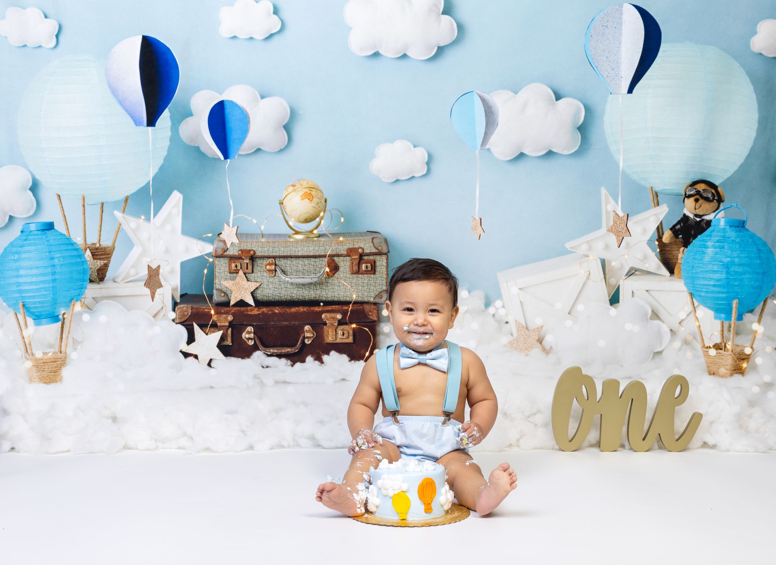 Baby during One Trip Around the Earth-themed cake smash in Glenview IL studio featuring hot air balloons, clouds, and travel-inspired decor.