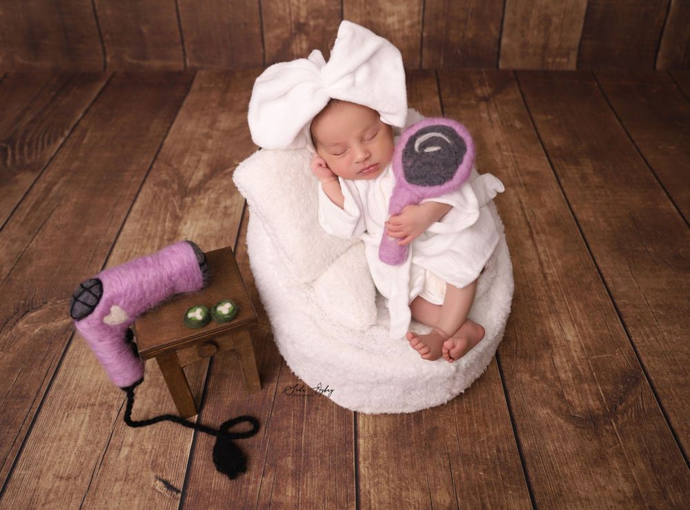 Newborn in white outfit posed with vintage hair dryers on wooden background.