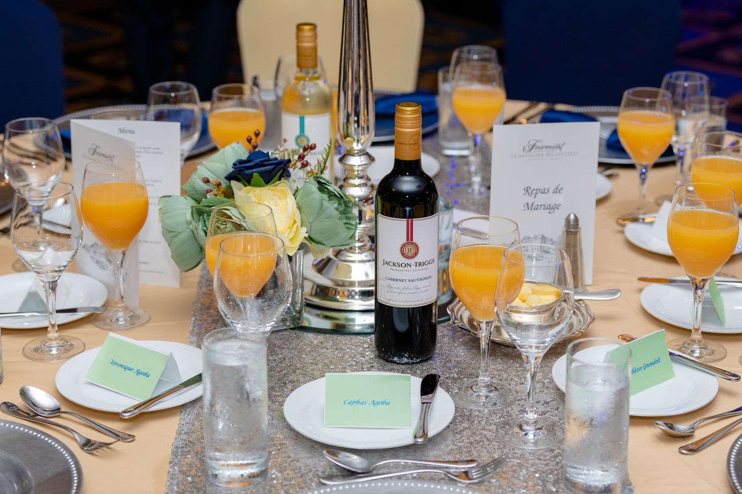 "Table de réception de mariage élégamment décorée avec vin, jus d'orange, fleurs et menus, capturée par Payo Studio."
