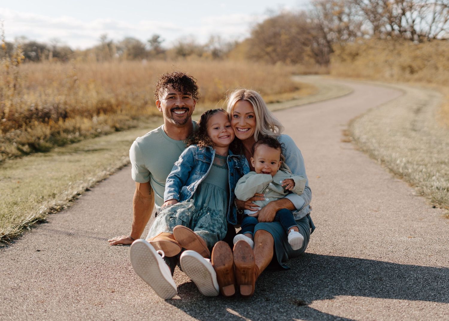 Family sitting together on paved trail during golden hour outdoor photo session.