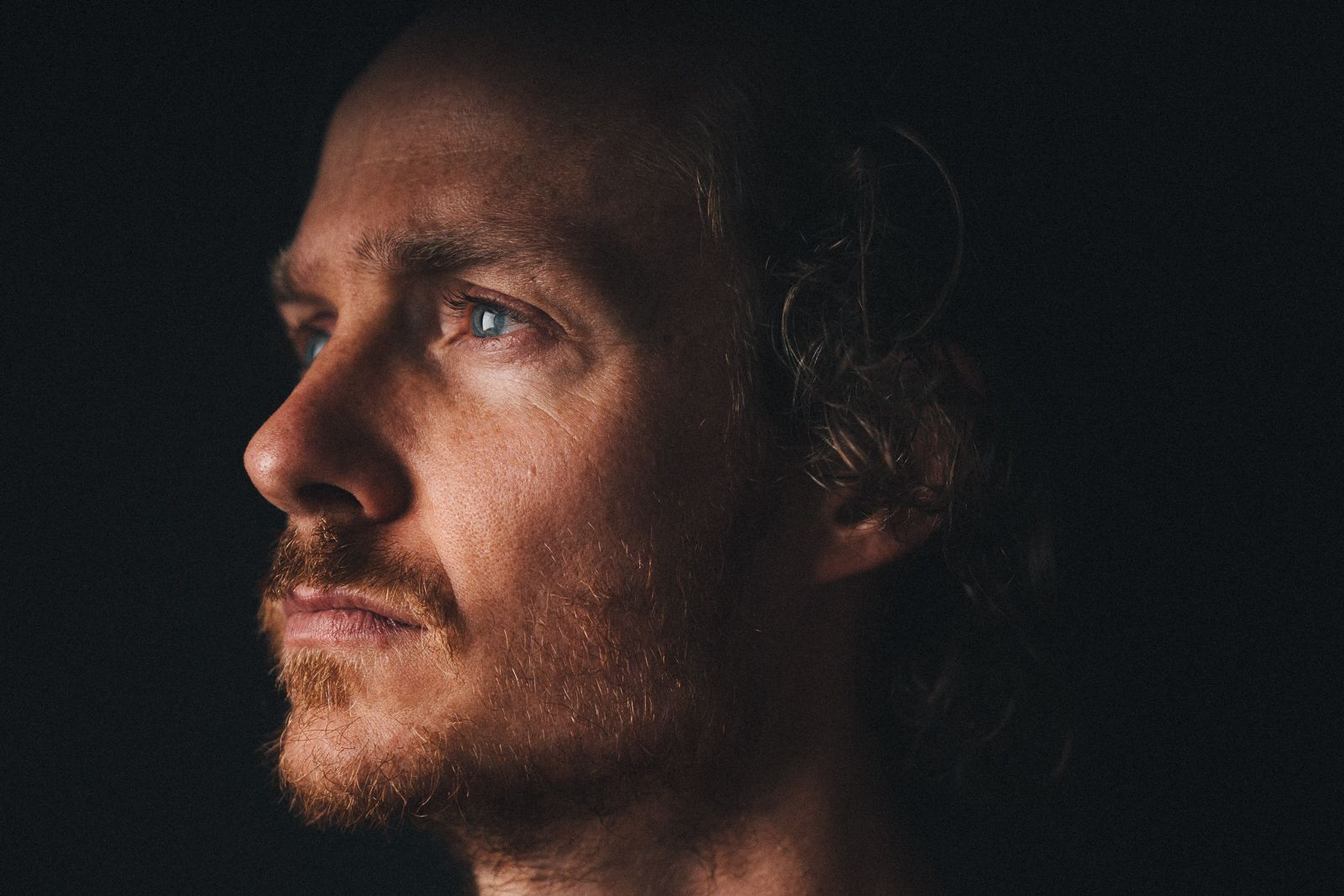 A dramatic side profile portrait with dramatic lighting shows facial features against a dark background.