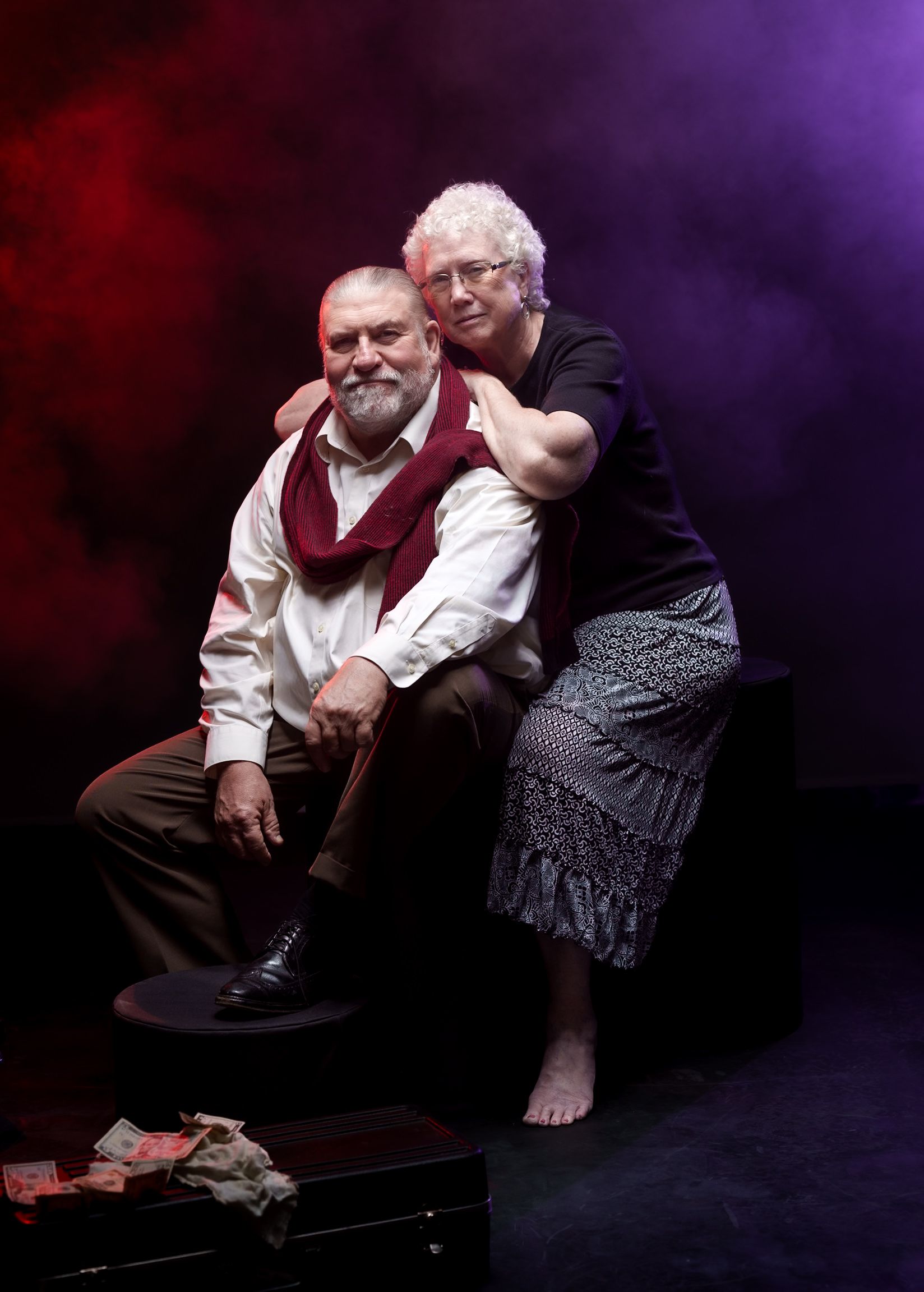 Intimate portrait of elderly couple posing against dramatic purple and red backdrop.