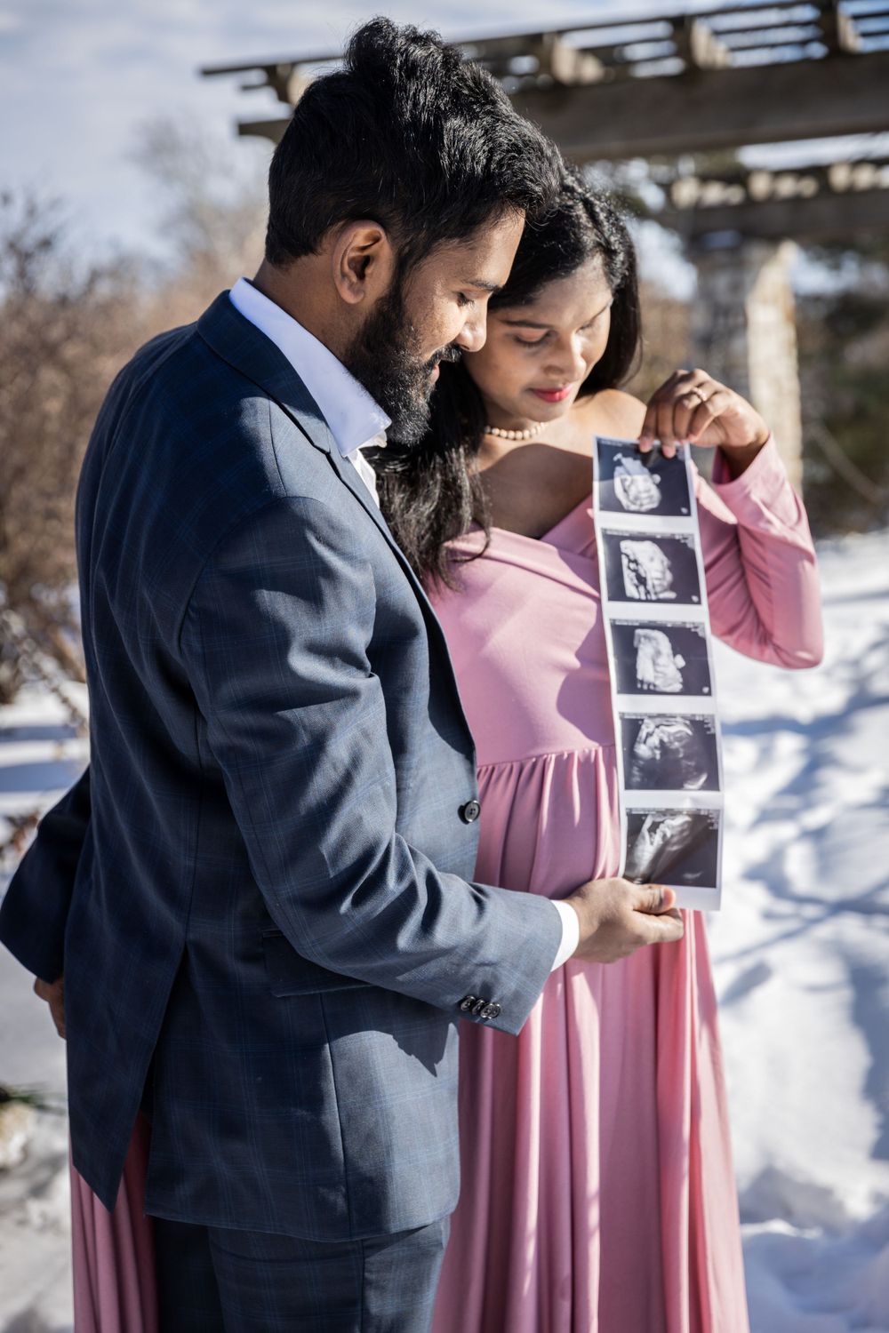 Couple in winter setting shares ultrasound photos during pregnancy announcement shoot.
