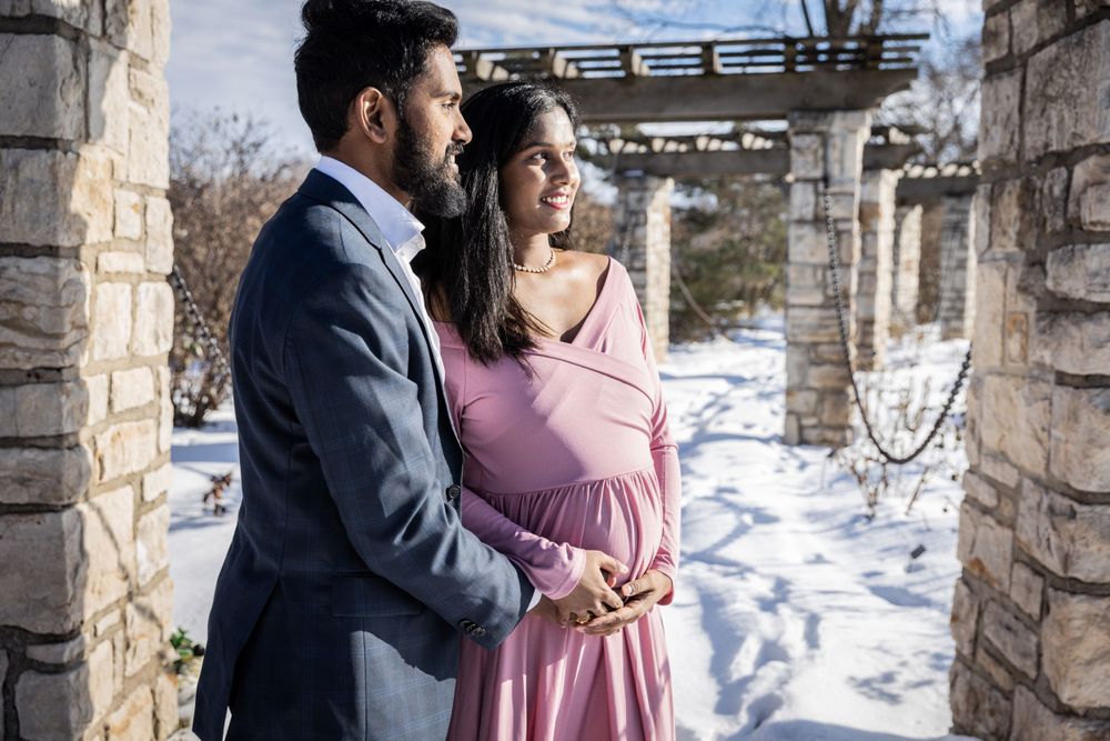 Couple embraces in snowy setting with stone architecture in background.