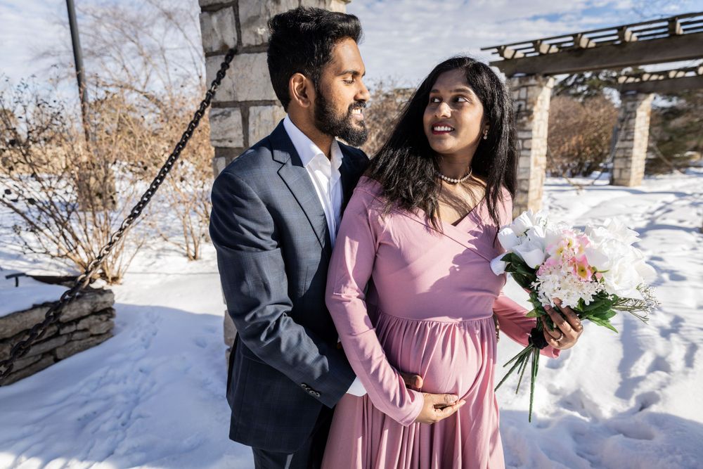 Winter maternity photoshoot features couple in formal wear against snowy landscape.
