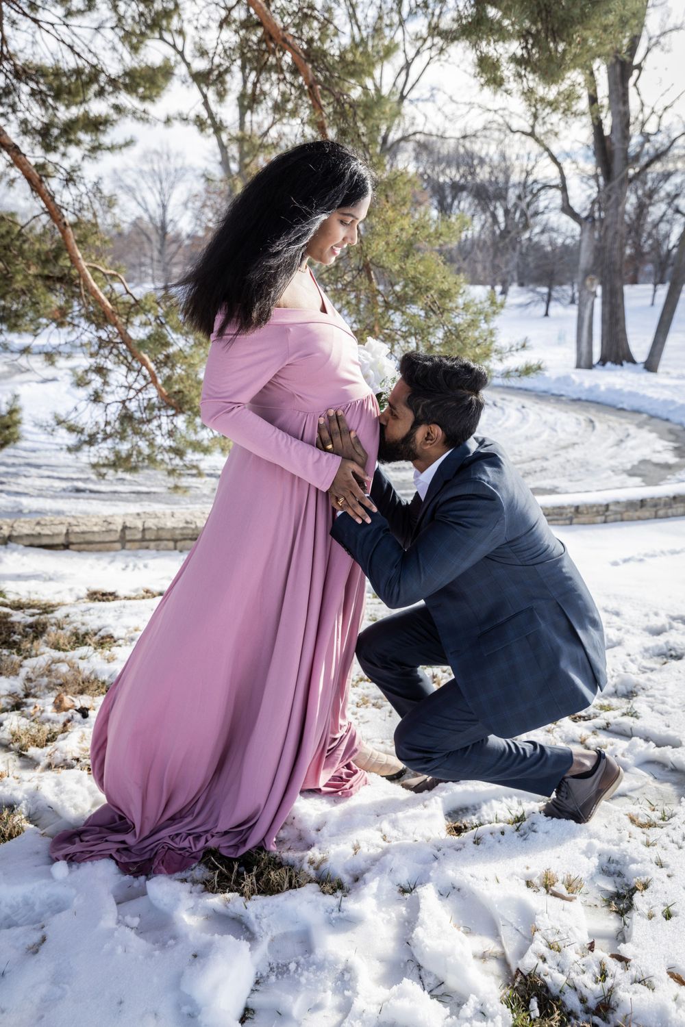 Romantic winter maternity photos captured in snow-covered park setting.