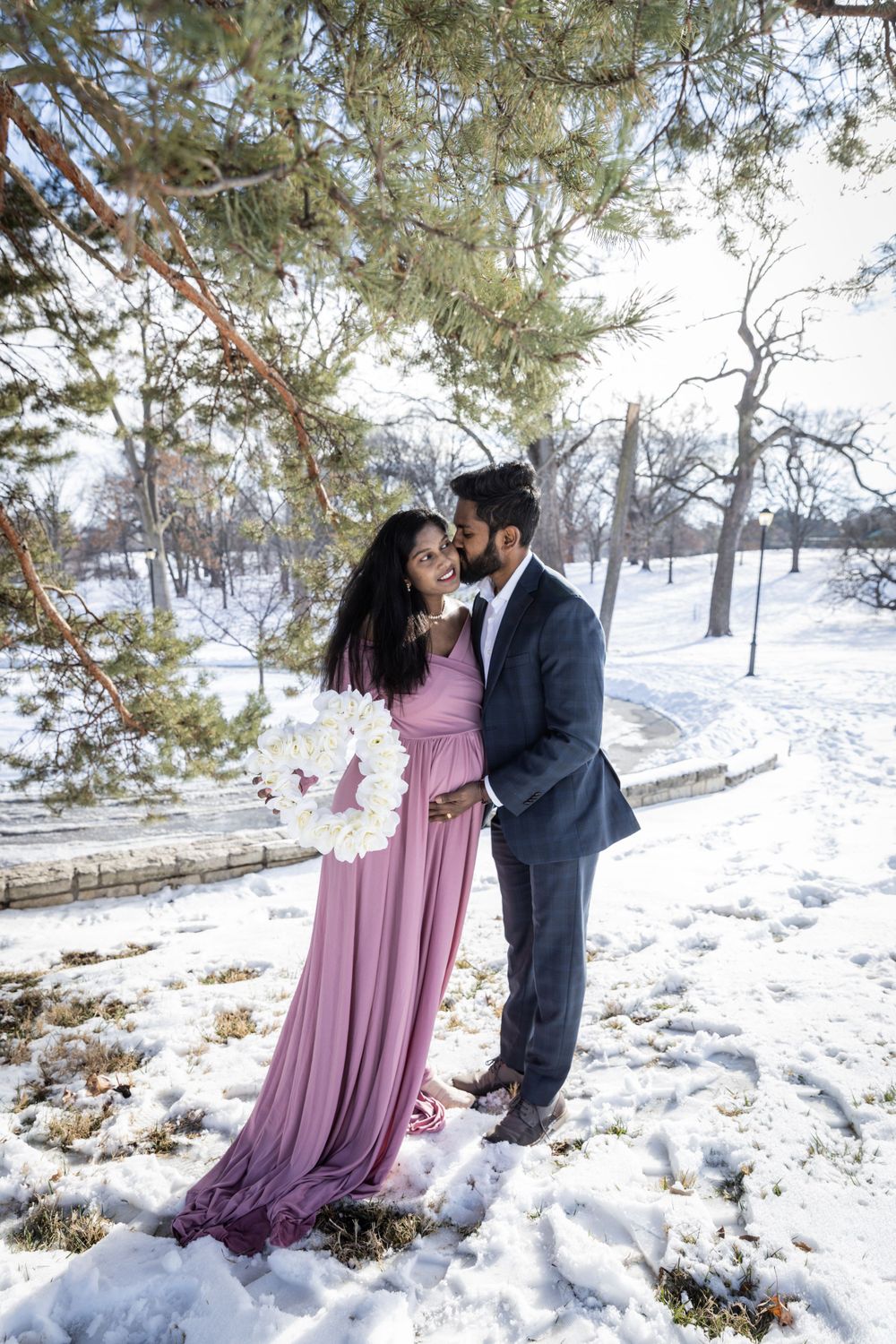 Winter maternity session features couple in formal wear against snowy landscape.