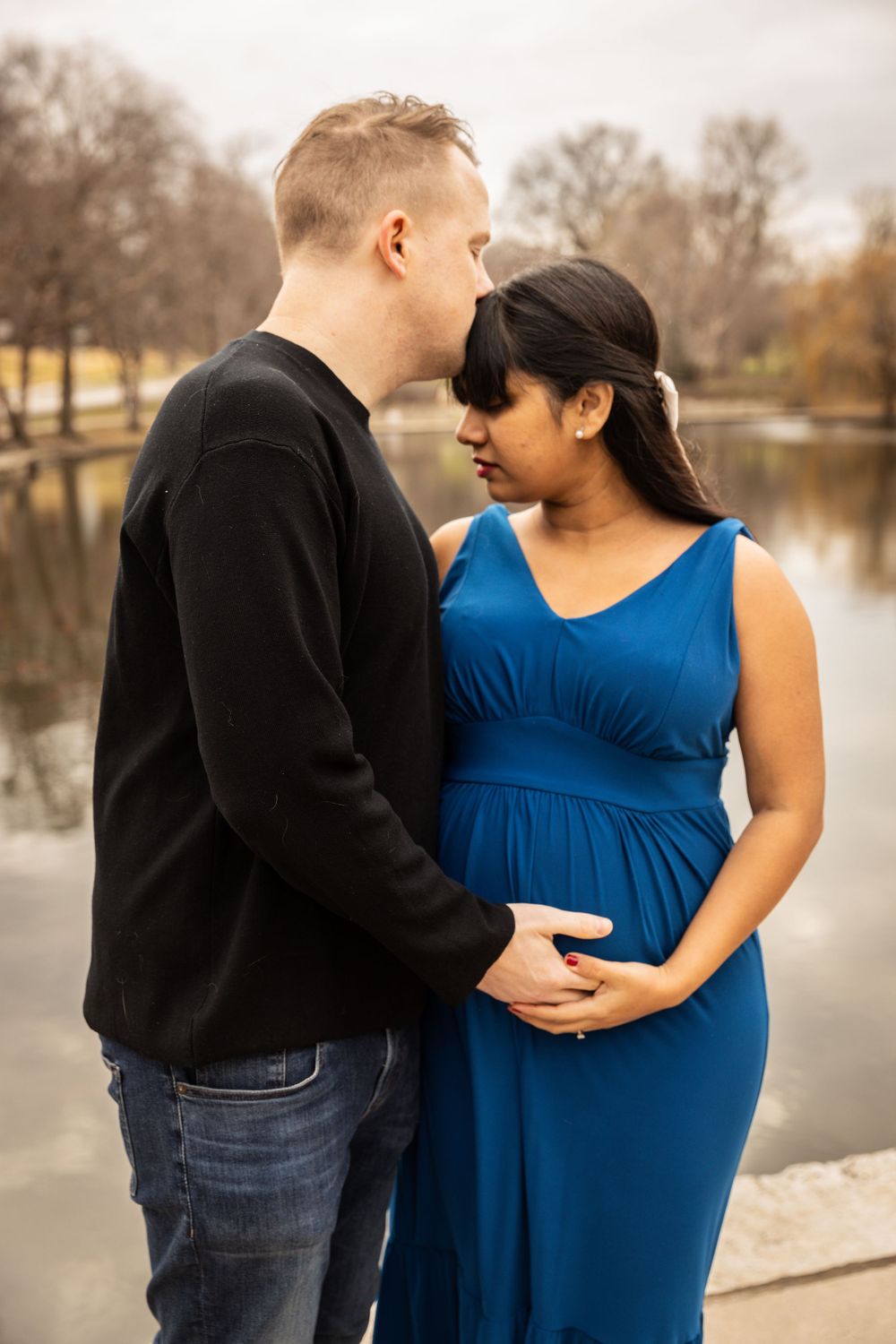 Couple poses together by lake during winter maternity session.