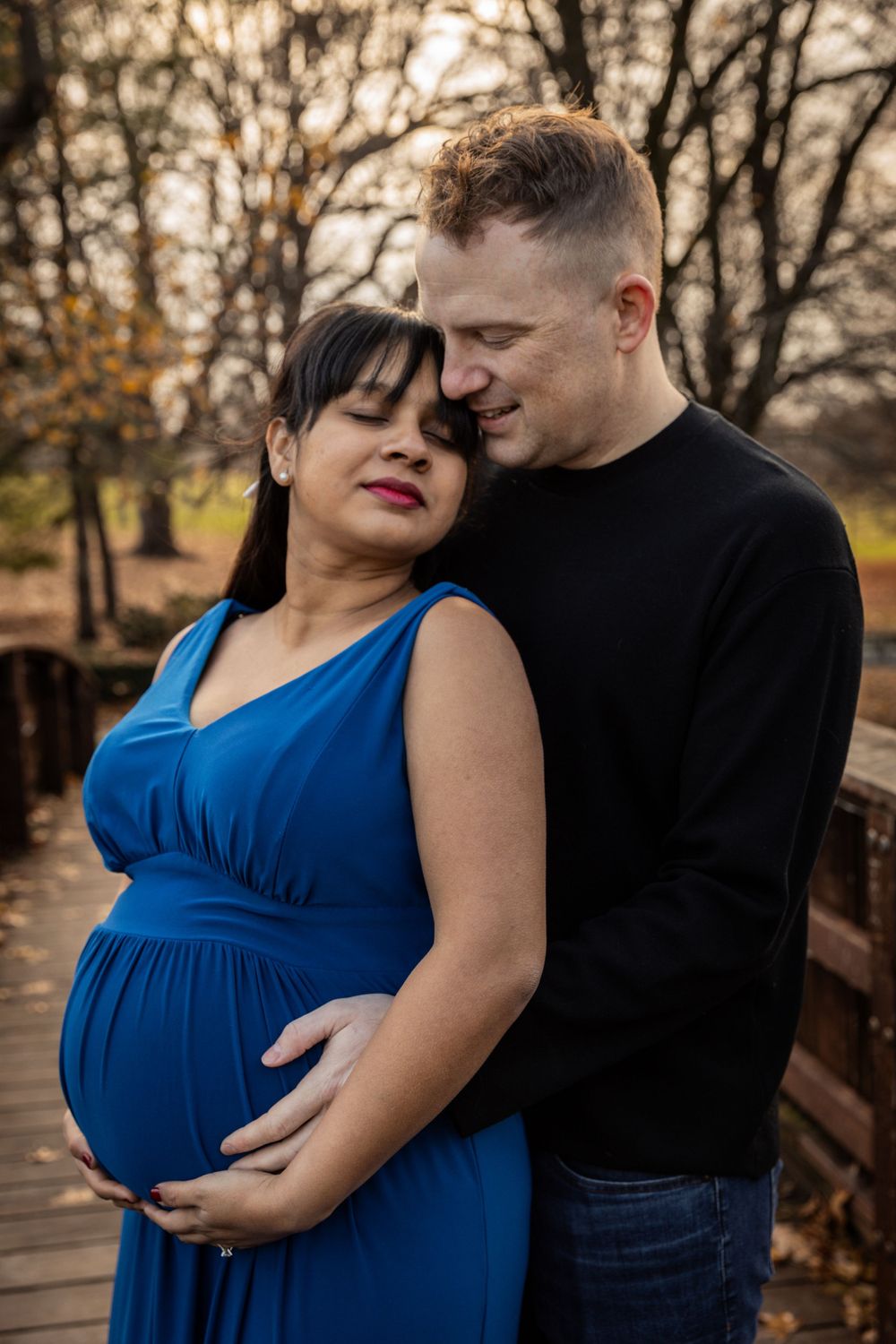 Expecting couple embraces on wooden bridge during autumn maternity photoshoot.